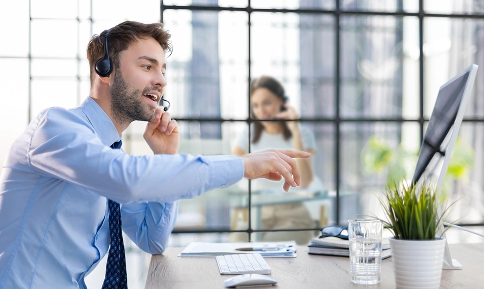 cheerful-young-support-phone-male-operator-headset-workplace-with-collegues-background-while-using-computer-help-service-client-consulting-call-center-concept cheerful-young-support-phone-male-operator-headset-workplace-with-collegues-background-while-using-computer-help-service-client-consulting-call-center-concept